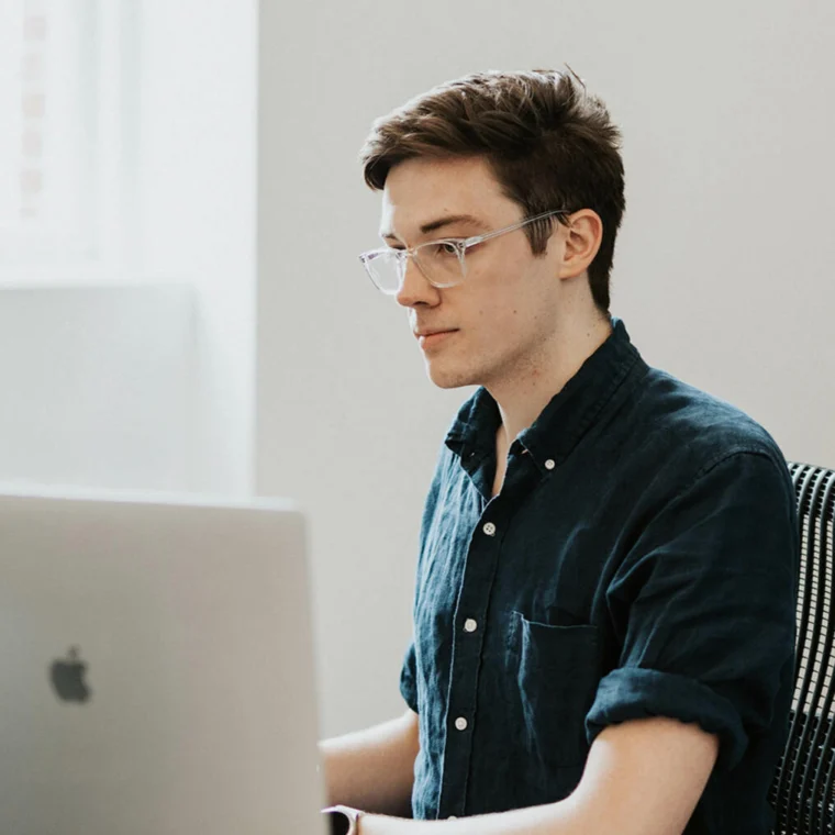 Person wearing glasses and a dark shirt, working on a laptop at a desk.
