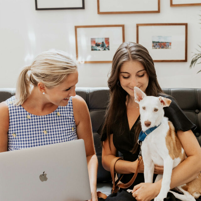 Two female coworkers sitting together with a dog.