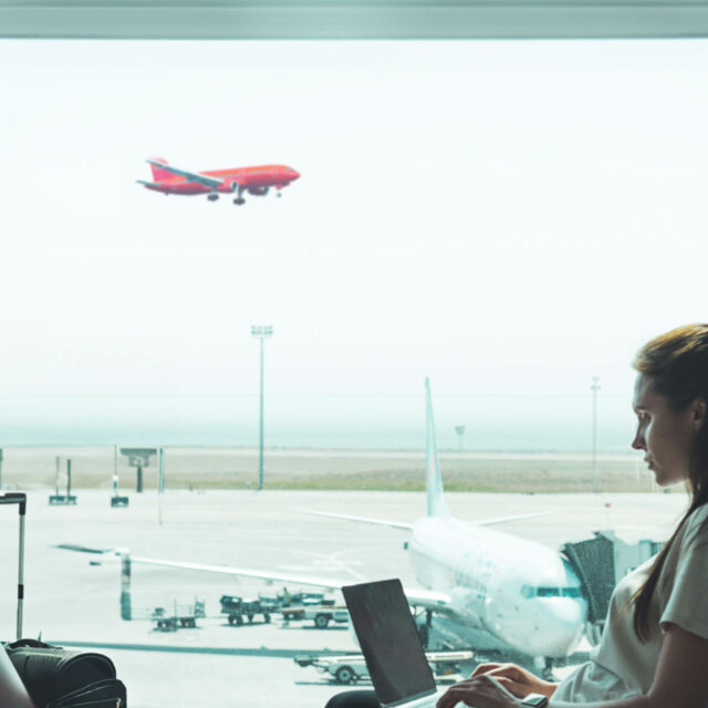 Woman on her laptop sitting at an airport with a plane landing outside the window.