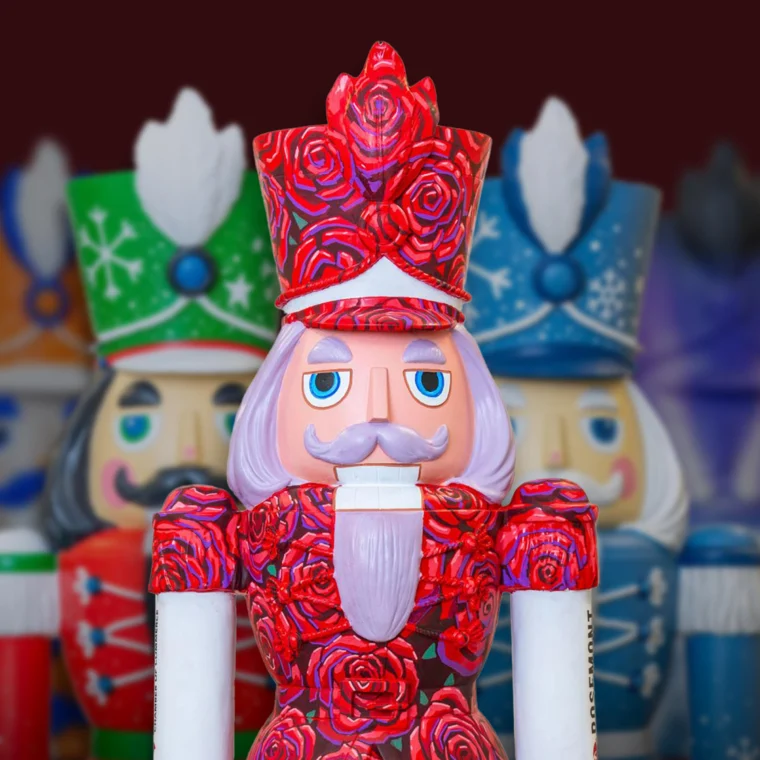 A painted nutcracker figurine with a red rose design stands in front of other colorful nutcracker figures, featuring blue eyes, a mustache, and a red crown.