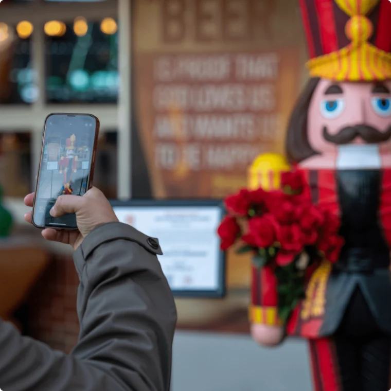 Person taking a photo of a nutcracker statue holding red flowers.