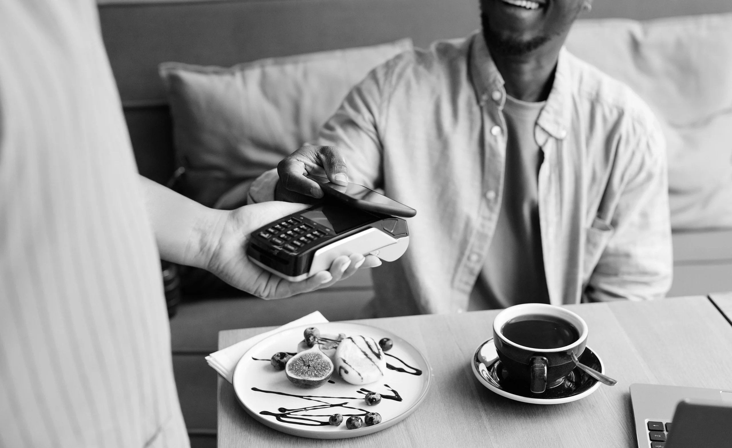 Person using a smartphone for contactless payment at a cafe. A cup of coffee and a dessert are on the table.