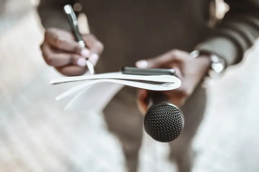 A person taking notes while holding a microphone.