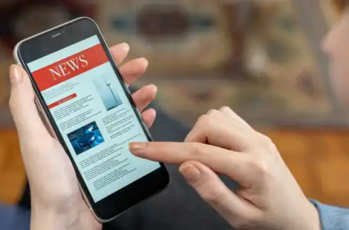 A person holding a smartphone with a news app open.