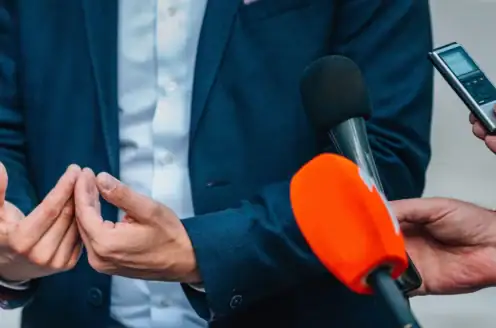A person speaking to people with multiple microphones in front.