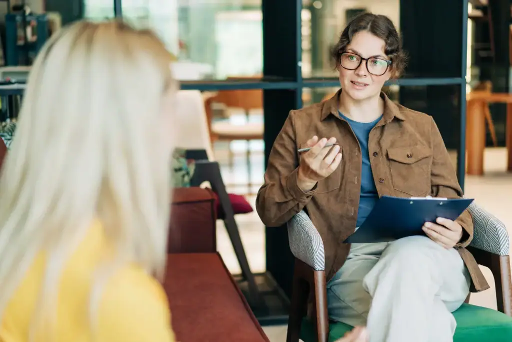 A woman speaking to another person while holding a clipboard and pen.