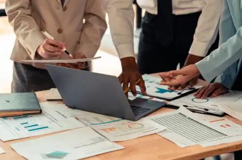 A group of people examining printed documents and a laptop together.