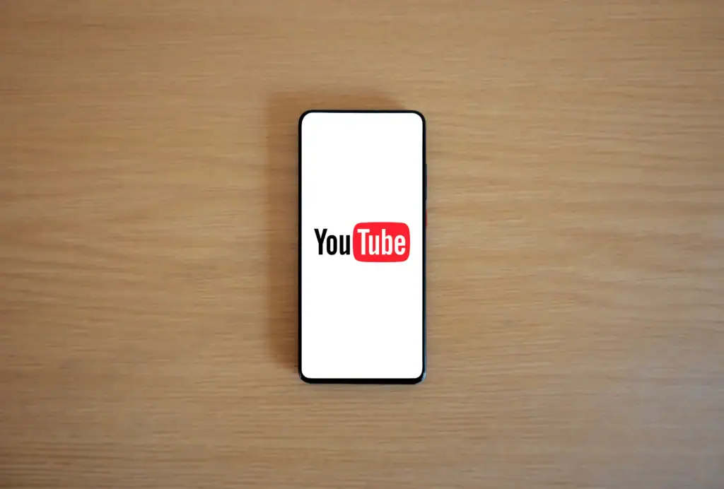 A smartphone with the YouTube logo displayed on its screen is placed on a wooden surface.