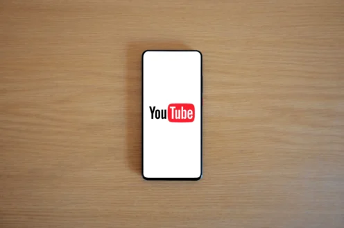 A smartphone with the YouTube logo displayed on its screen is placed on a wooden surface.